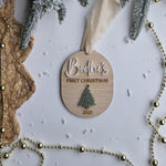 Wooden ornament with 'Bodhi's First Christmas 2023' text, surrounded by festive decorations on a white background.
