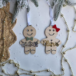 Two wooden gingerbread ornaments with names 'Charlie' and 'Olivia' hanging on a Christmas tree.