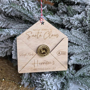 Wooden envelope-shaped ornament with 'Santa Claus' text, hanging on a Christmas tree.