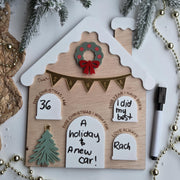 Wooden house-shaped ornament with Christmas decorations and text on a white background.