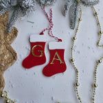 Red Christmas stockings with gold letters 'G' and 'A', surrounded by gold beads and snow-covered branches on a white background.