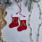 Red Christmas stockings with gold letters 'G' and 'A', surrounded by gold beads and snow-covered branches on a white background.