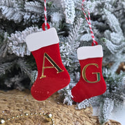 Two red Christmas stockings with gold letters 'A' and 'G' hanging on a decorated tree.