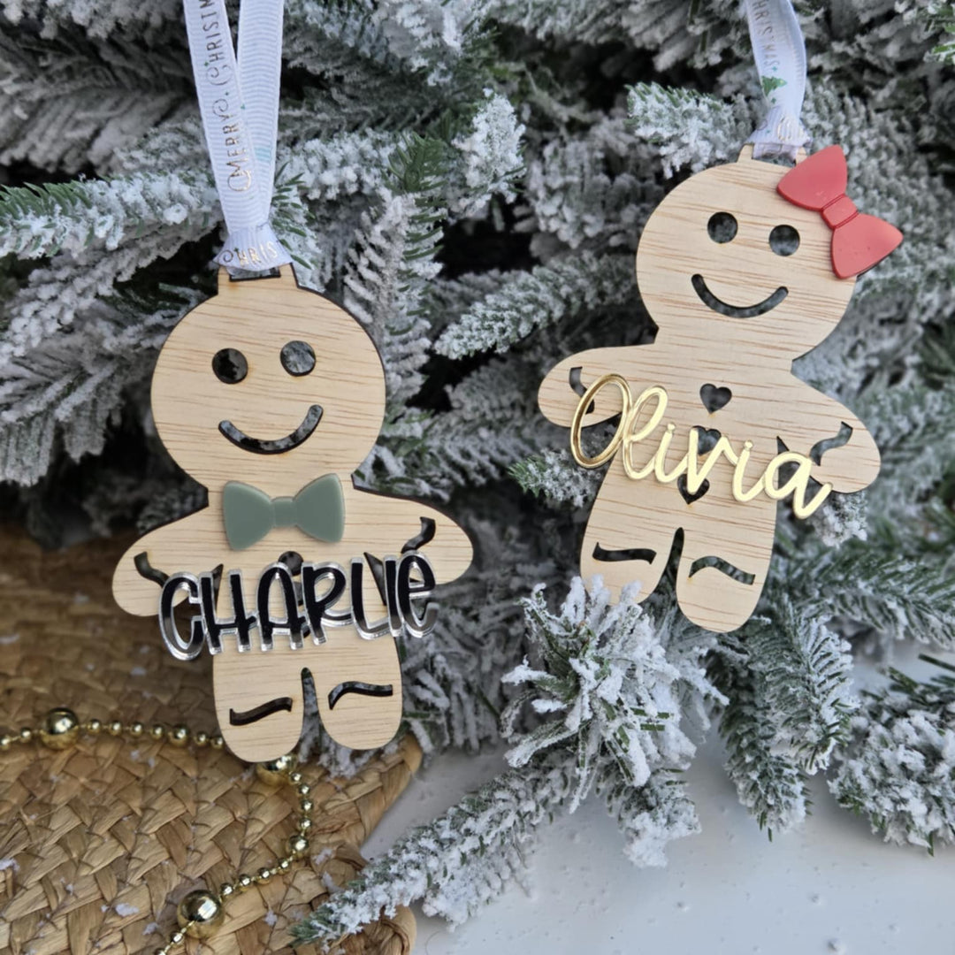 Two wooden gingerbread ornaments with names 'Charlie' and 'Olivia' hanging on a Christmas tree.