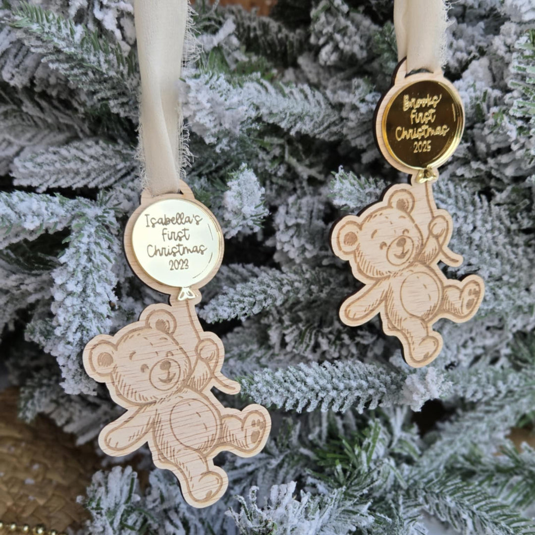 Two wooden teddy bear ornaments on a Christmas tree with engraved text.